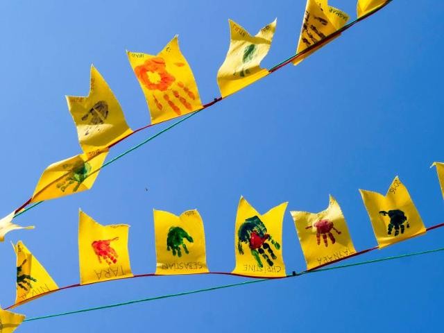 Gelbe Fahnen mit Kinderhandabdrücken vor blauem Himmel