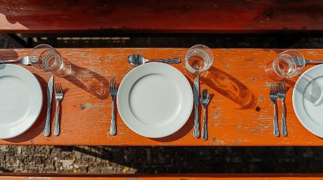 Bild von einfachen Gläsern und einfachem Besteck und weißen Tellern für eine Veranstaltung im Freien mit orangefarbenen Bierbänken